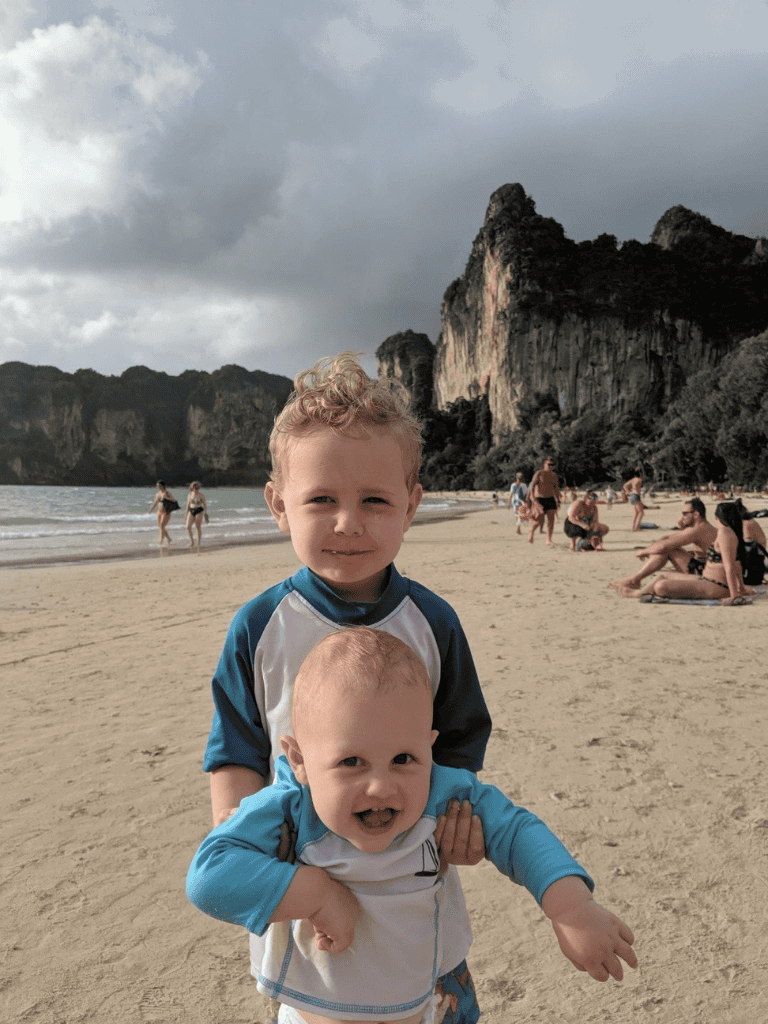 Ocean beach with children playing, scenic cliffs in the background, cloudy sky, family vacation destination.