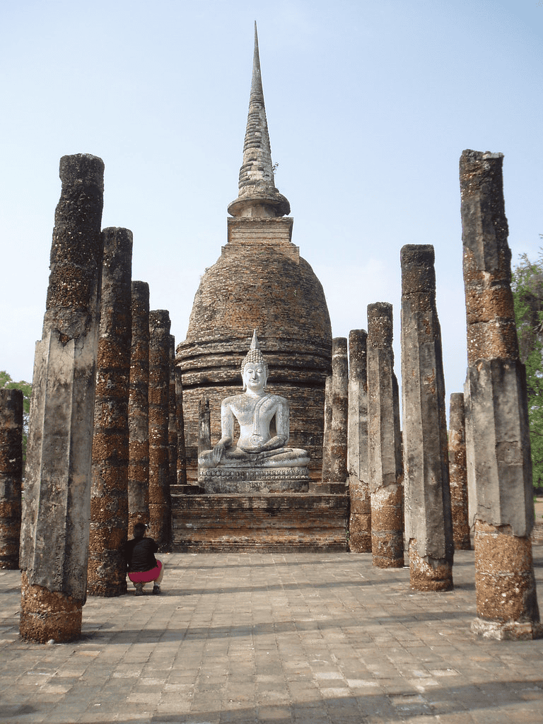 Ancient temple ruins with Buddha statue surrounded by stone columns in Thailand.