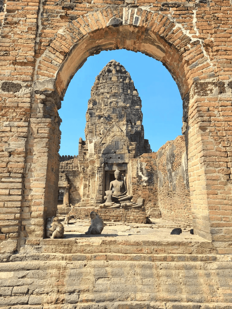 Ancient temple ruins with a Buddha statue and monkeys, in Thailand's historic site.