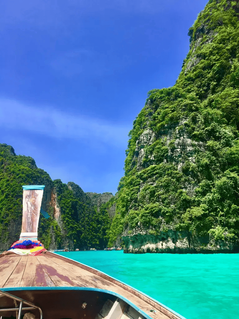 Vibrant tropical river cruise through lush green limestone cliffs in Thailand.