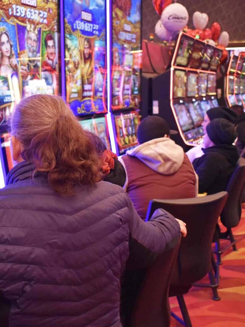 Unisex casino arcade with people playing slot machines, colorful lights, and vibrant gaming environment.