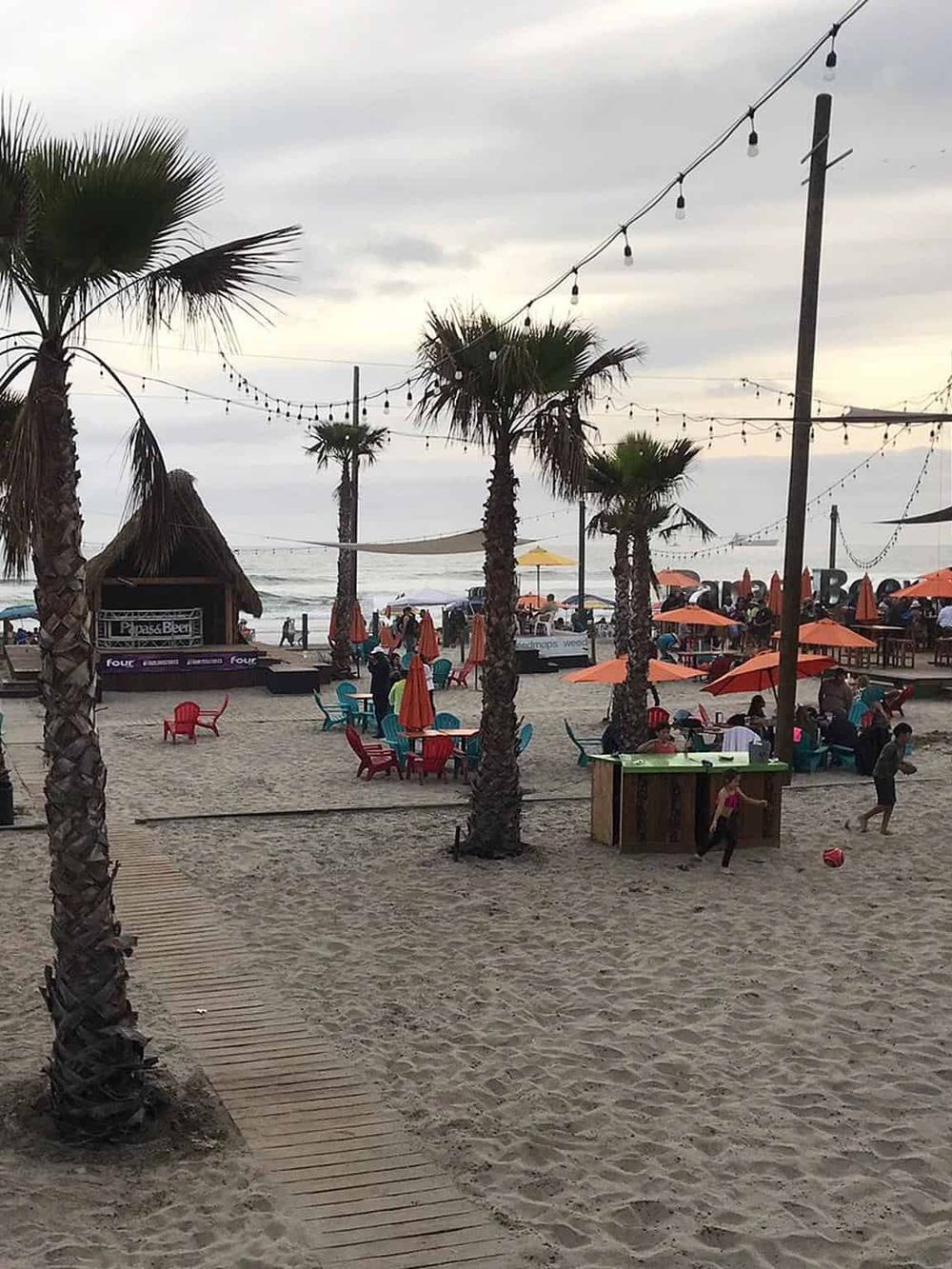 Colorful beachside venue with palm trees, string lights, and vibrant seating for outdoor dining and entertainment.