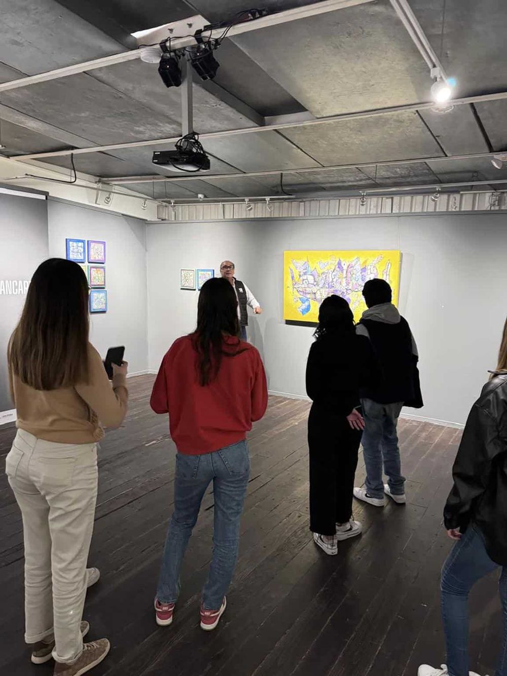 Colorful art gallery with visitors viewing artwork and a guide explaining pieces.