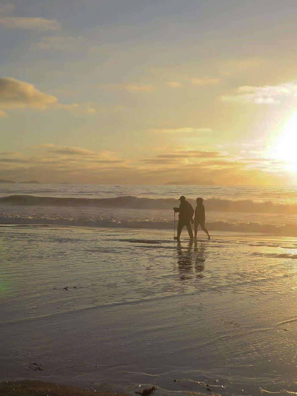 Sunset beach walk with two people, ocean view and warm golden sunlight, perfect for relaxation and seaside exploration.