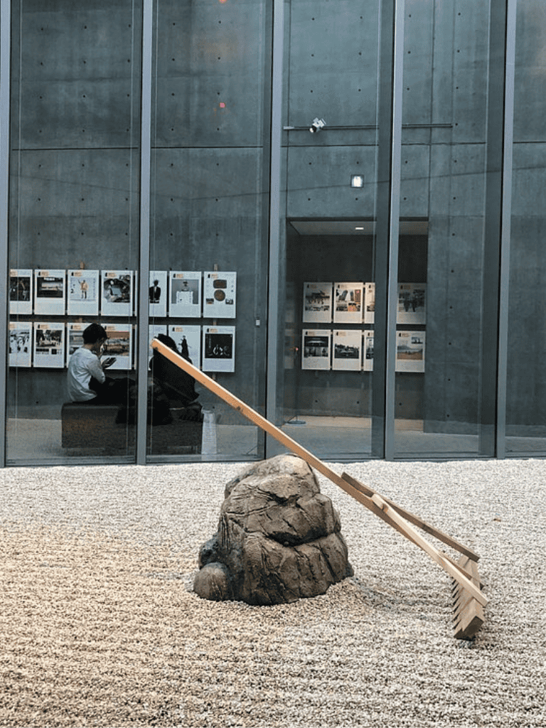 Aesthetic outdoor sculpture of a rake leaning against a rock in a modern urban setting.
