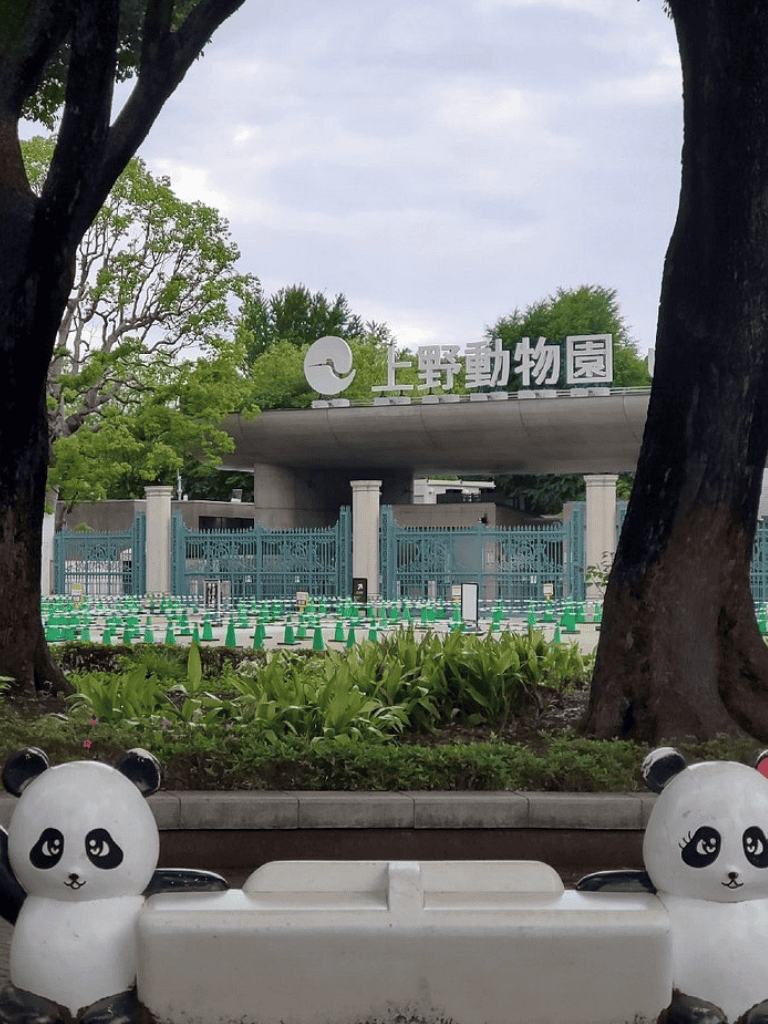 Cute panda statue at Ueno Zoo entrance in Tokyo, Japan, with greenery and zoo signage in the background.