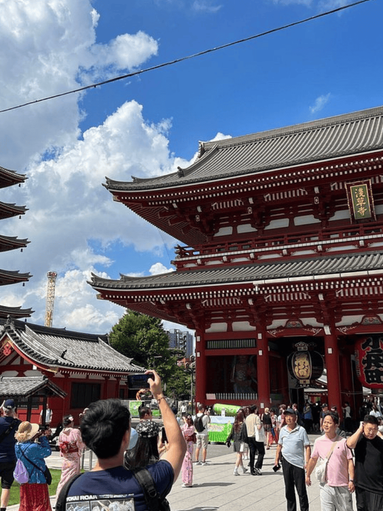 Colorful traditional Japanese temple in Tokyo with visitors taking photos, under a bright blue sky.