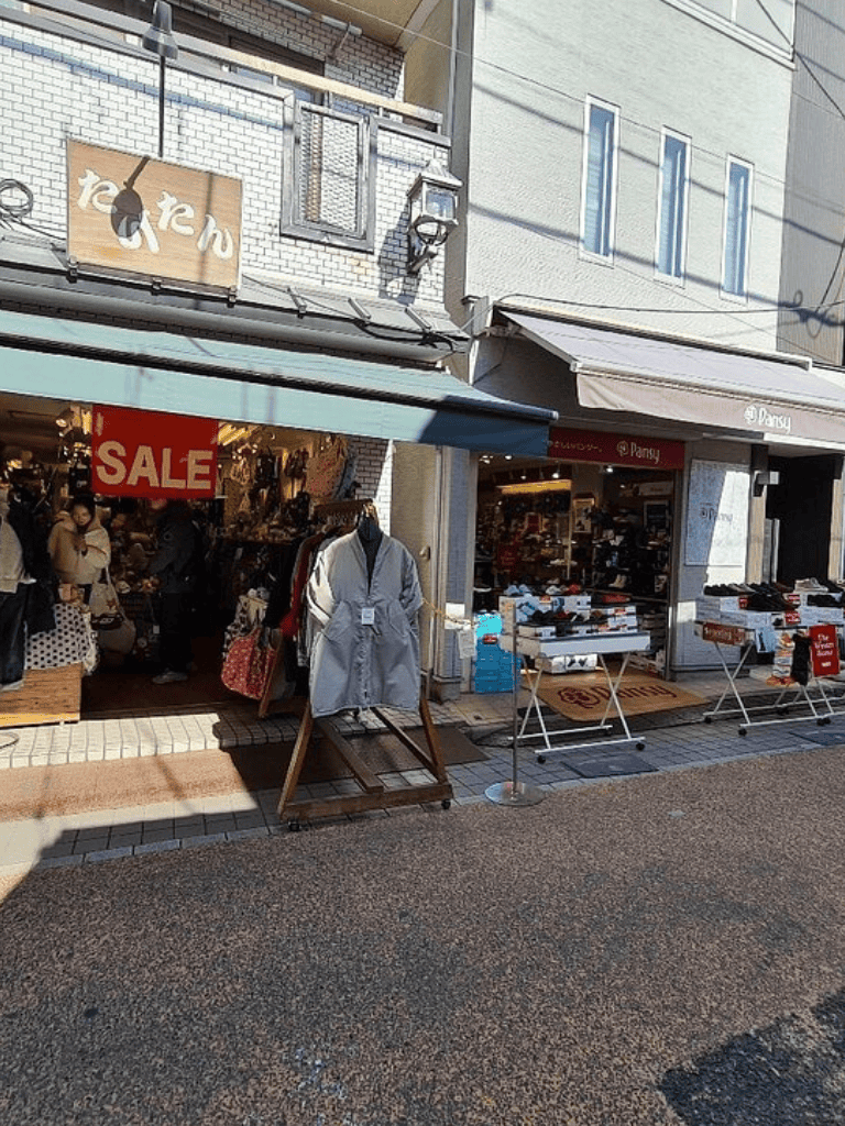 Bright storefronts showcasing sale clothing and accessories at QuestForDirections shopping district in Japan.