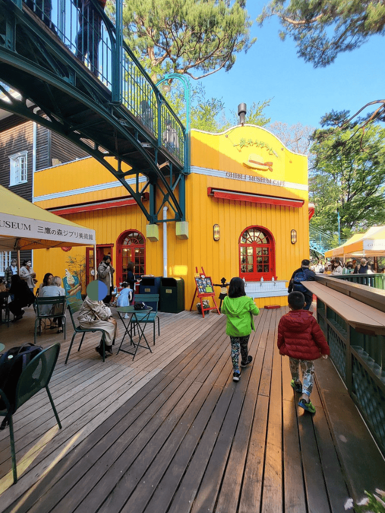 Colorful museum cafe and outdoor seating area with children and visitors in a park setting.