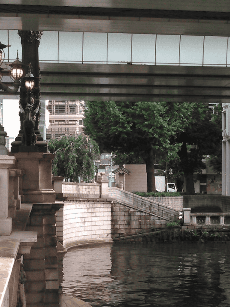 Elegant cityscape under a bridge with water, trees, and historic architecture, ideal for exploring urban waterfronts.