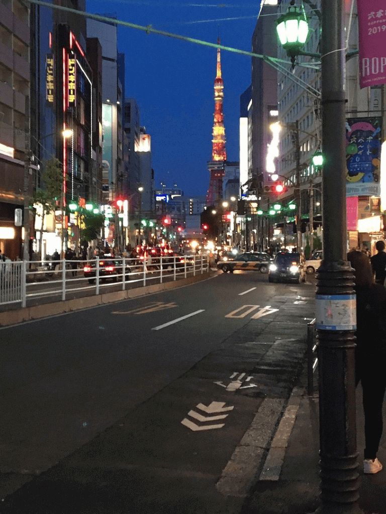 Tokyo city street scene at night with illuminated buildings and Tokyo Tower in the background, vibrant urban atmosphere.