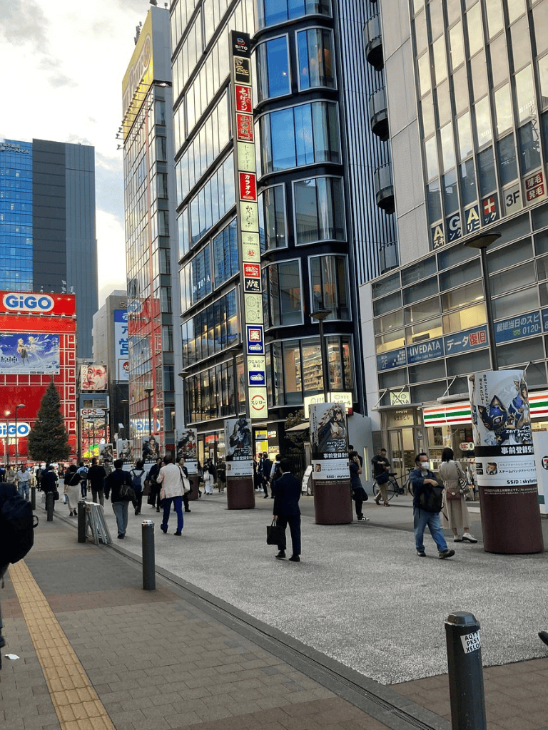 Busy city street scene with modern glass buildings and pedestrians in an urban commercial district.