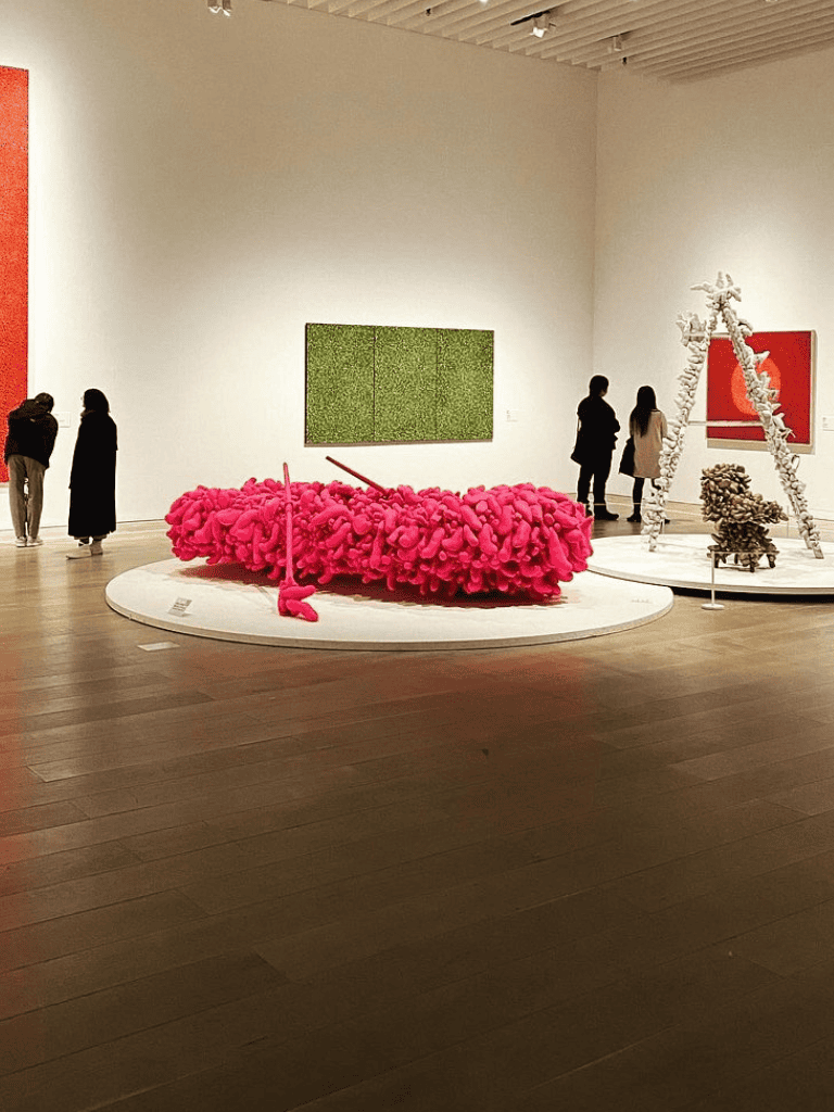 Pink fuzzy art installation in modern art gallery with viewers observing exhibits.
