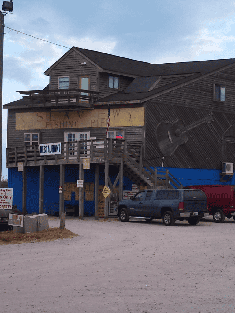 Fishing pier restaurant on a rustic wooden building with large guitar mural and parking lot.