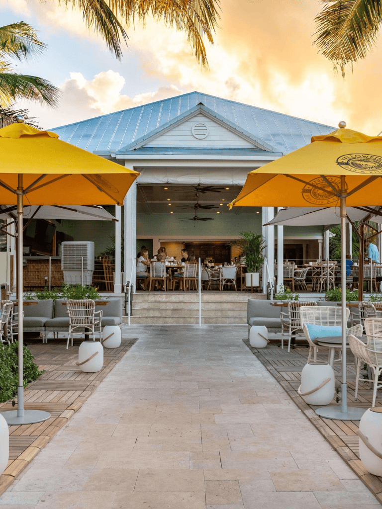 Outdoor dining area at Quest for Directions restaurant with yellow umbrellas, tropical setting, and sunset sky.