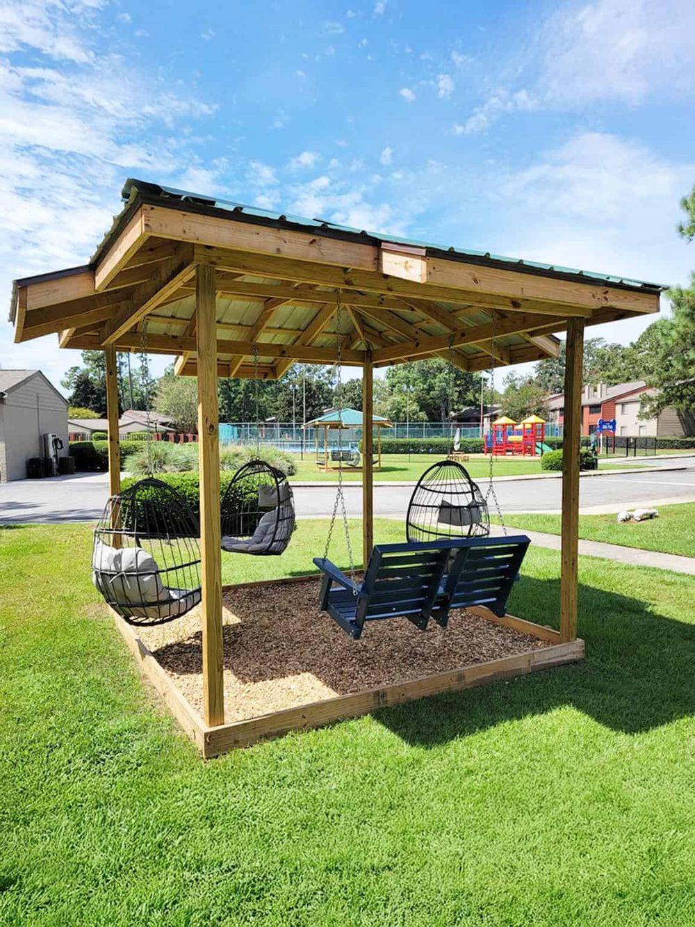 Outdoor swing pavilion with cozy hanging chairs in a sunny park setting for relaxation and outdoor fun.