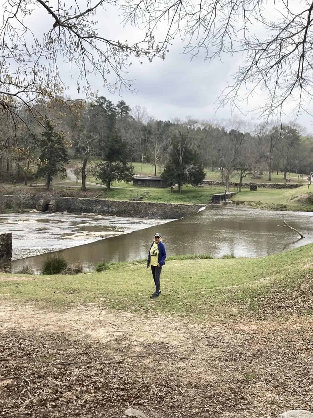 Quiet park with river, trees, and person enjoying outdoor scenery - perfect for nature walks and relaxation.