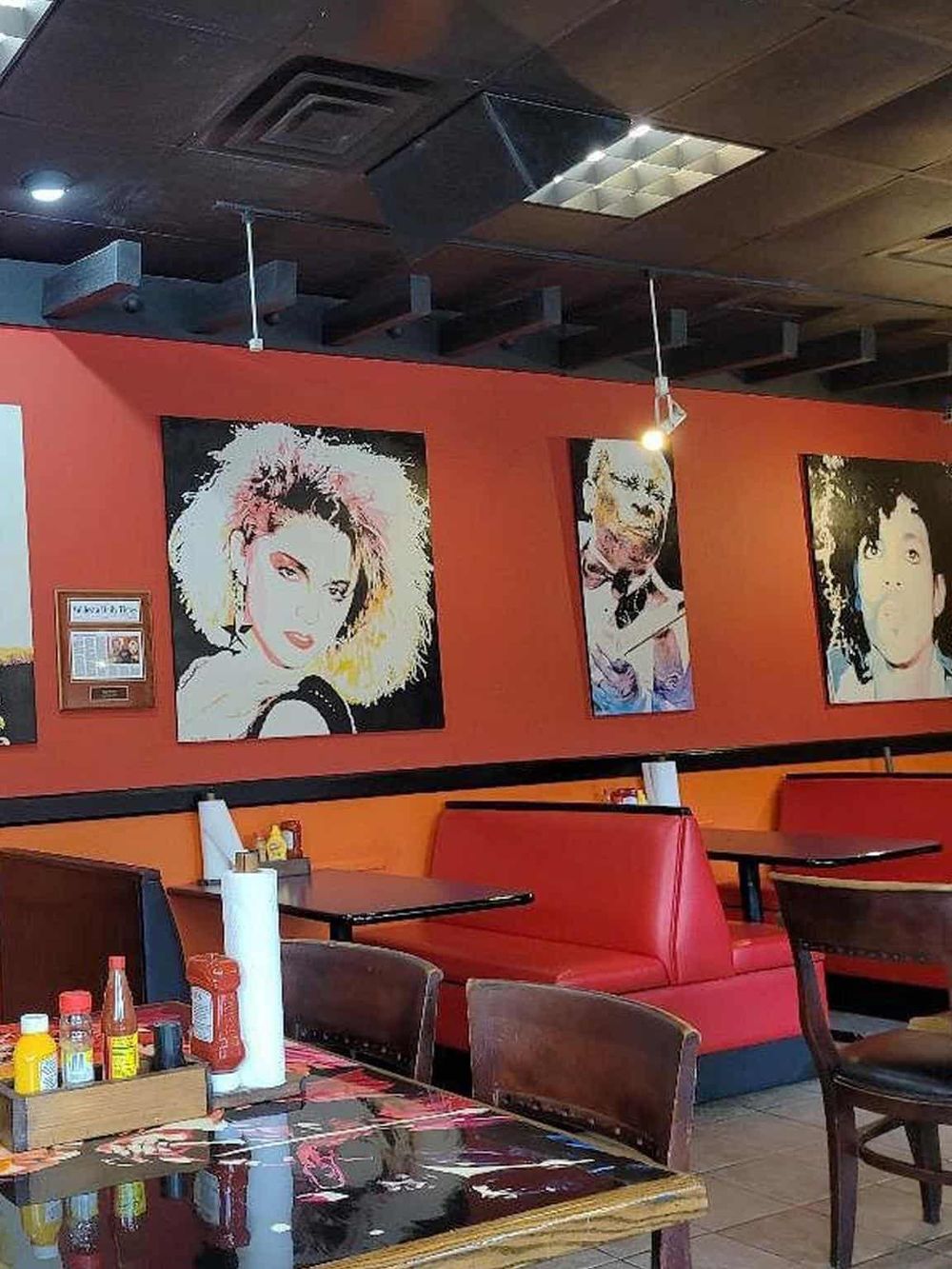 Colorful artwork portraits in a vibrant restaurant decor with red booths and cozy seating.