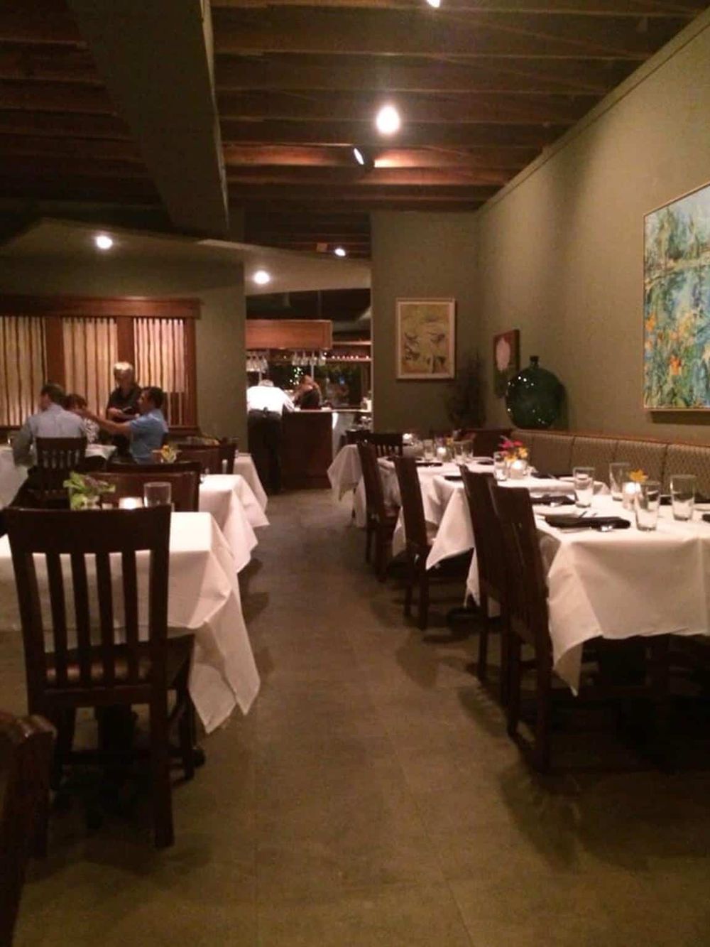 Elegant restaurant interior with white tablecloths and wooden chairs for fine dining, featuring muted lighting and cozy ambiance.