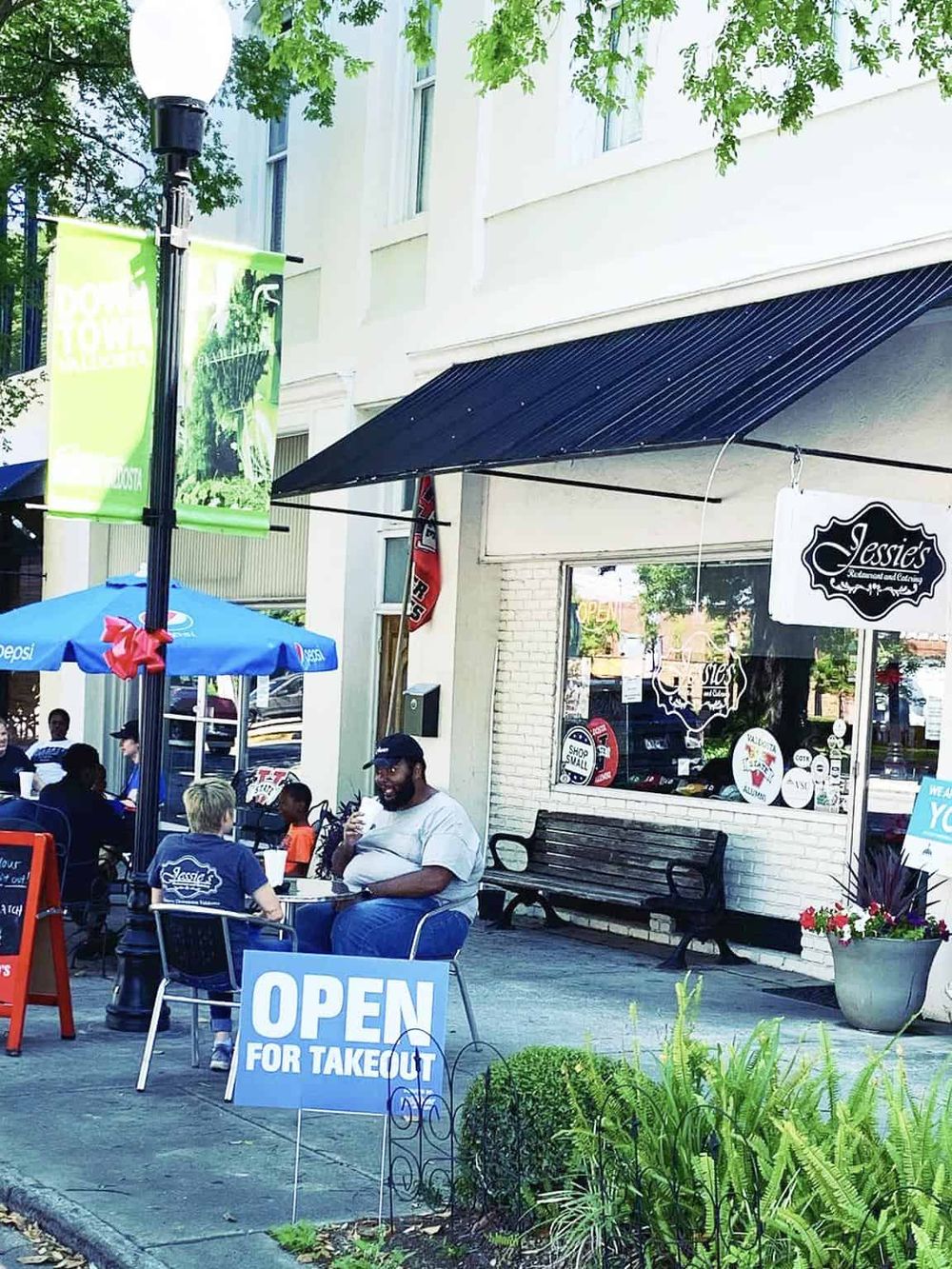 Outdoor dining at Quest for Directions restaurant, with "Open for Takeout" sign and cafe seating.