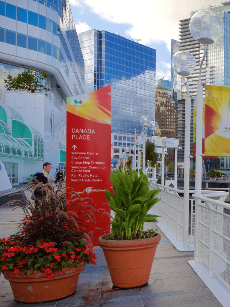 Bright Vancouver downtown waterfront with modern buildings and "Canada Place" signage, busy with tourists and visitors.