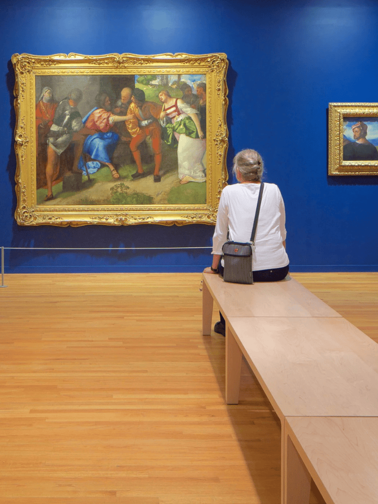 1. Woman observing classic artwork in art museum, blue wall background.
