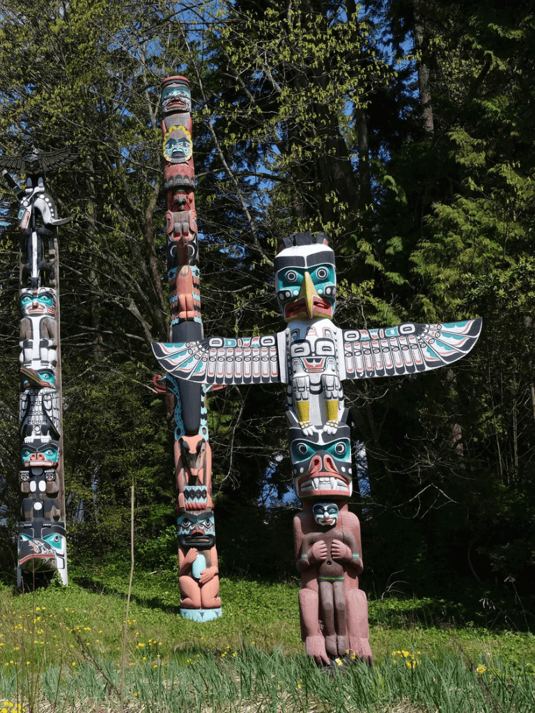Colorful Native American totem poles in lush forest setting for cultural tourism and indigenous art exploration.