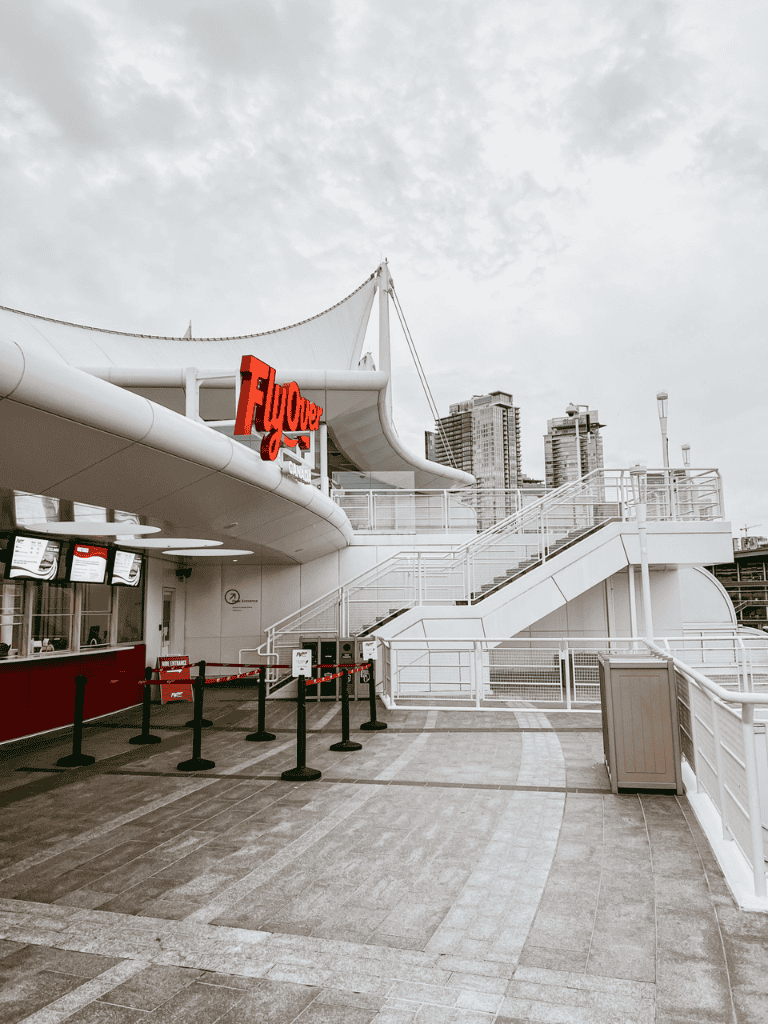 Empty outdoor Quest for Directions terminal at a city harbor with modern buildings, sky, and queue barriers.