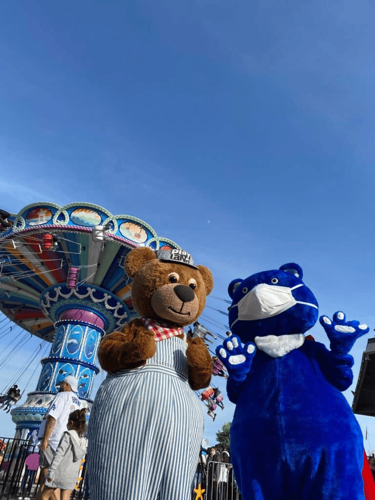Cute bear and blue mascot wearing face masks at amusement park, family fun, and carnival attractions.