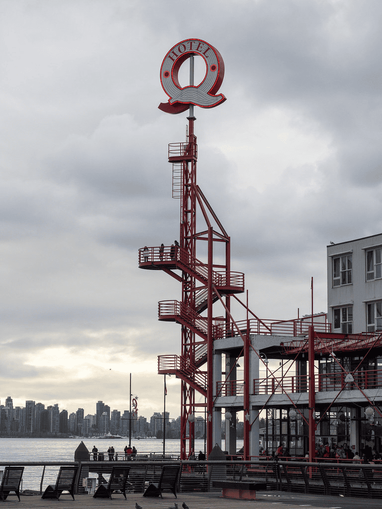 Colorful hotel sign on tall red steel structure overlooking city skyline and water.