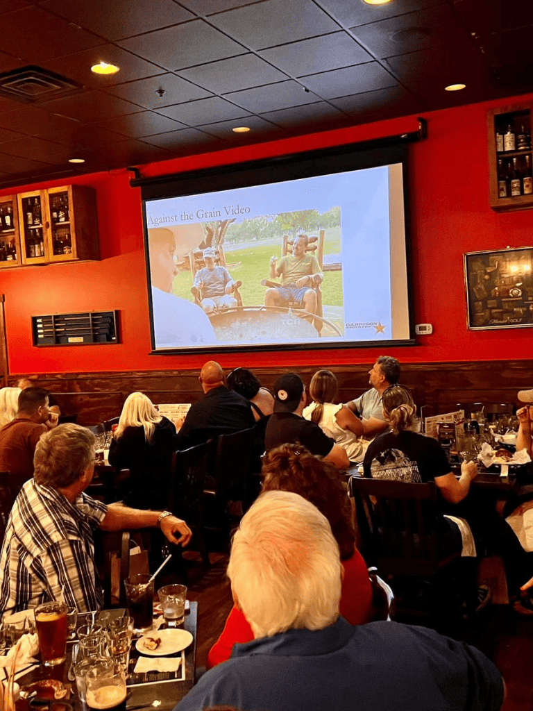 Enjoying an indoor viewing event at a restaurant or pub with a group watching a presentation on a large screen.