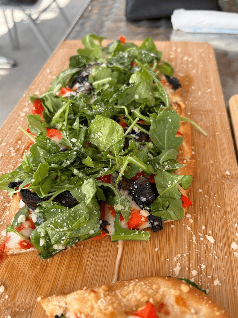 Fresh arugula and vegetable pizza on wooden serving board, farm-to-table experience.