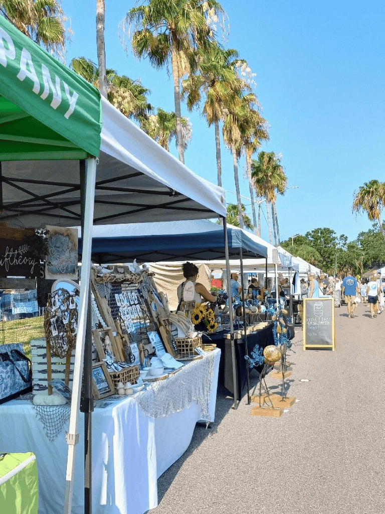Colorful outdoor market stalls at a sunny event with palm trees in the background.