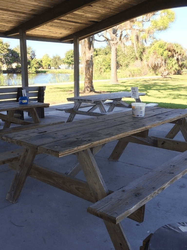 1. Wooden picnic tables under a pavilion by a scenic lake in outdoor park area.