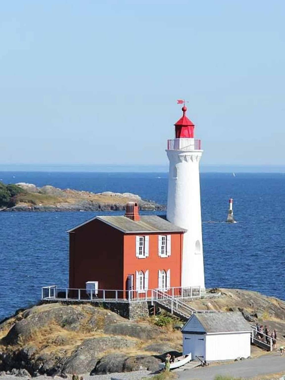 Colorful lighthouse on rocky coast with ocean view, popular travel destination and scenic seaside spot.