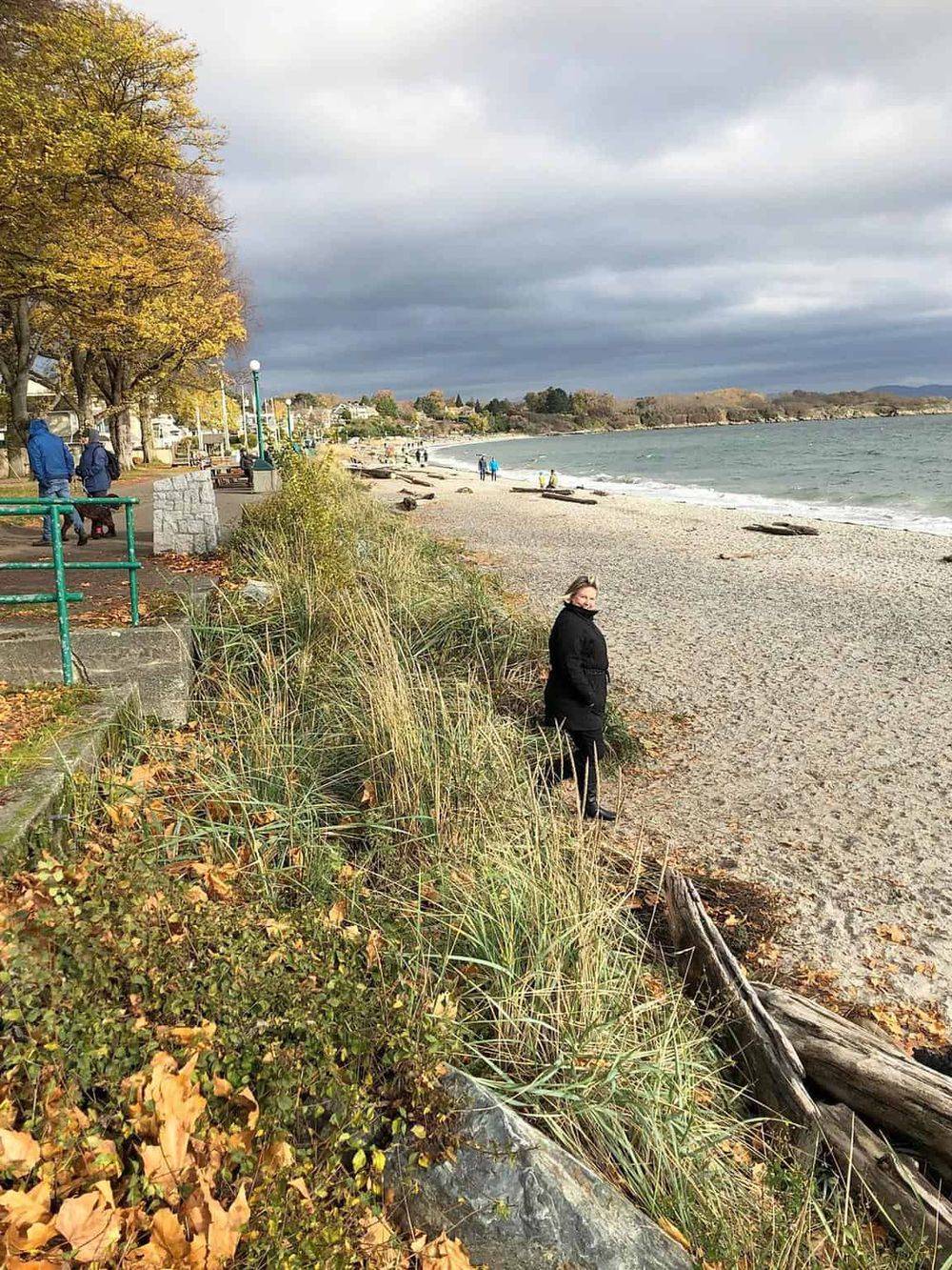 Scenic beach with walking path, autumn trees, and people enjoying seaside views in Oregon.