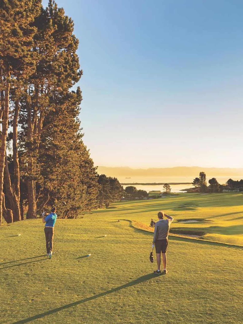 1. Scenic golf course at sunset with two players near trees and water.