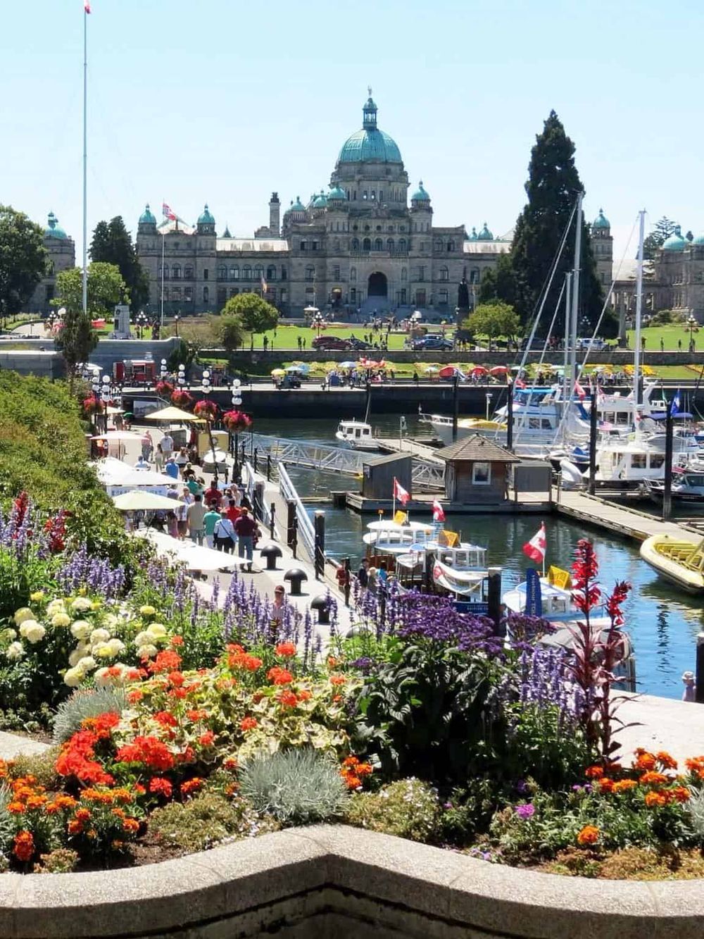 Beautiful harbor with boats, vibrant flowers, and the British Columbia Parliament Building in Victoria, Canada.