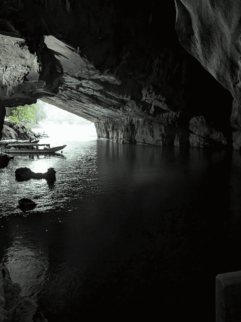 Serene river cave with boat access and dramatic rock formations under natural lighting.