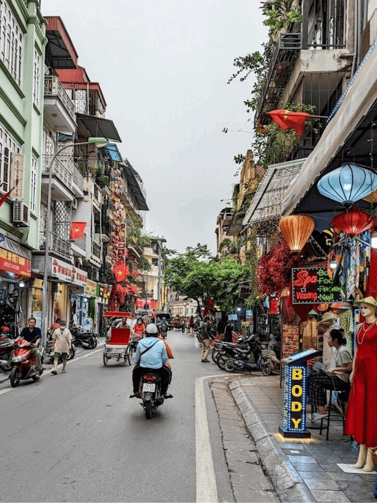 Bike and scooter traffic on busy street in Hanoi, Vietnam, lined with shops, eateries, and vibrant decor.