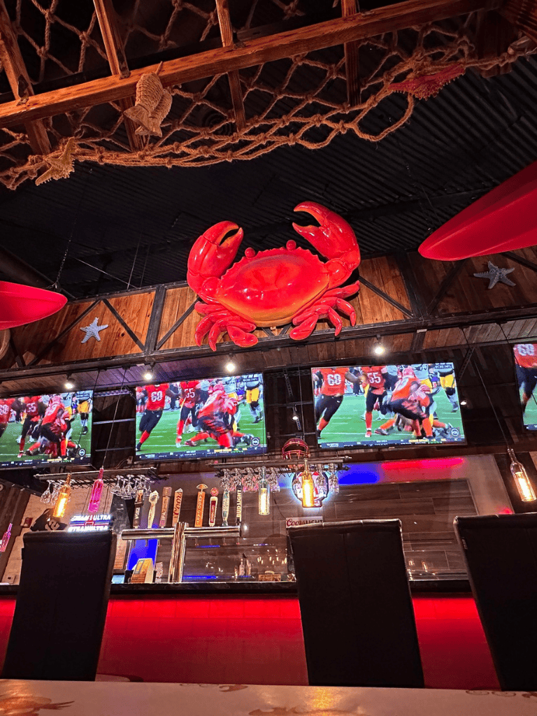 Crab decoration hanging from ceiling inside a sports bar with multiple TV screens showing football.