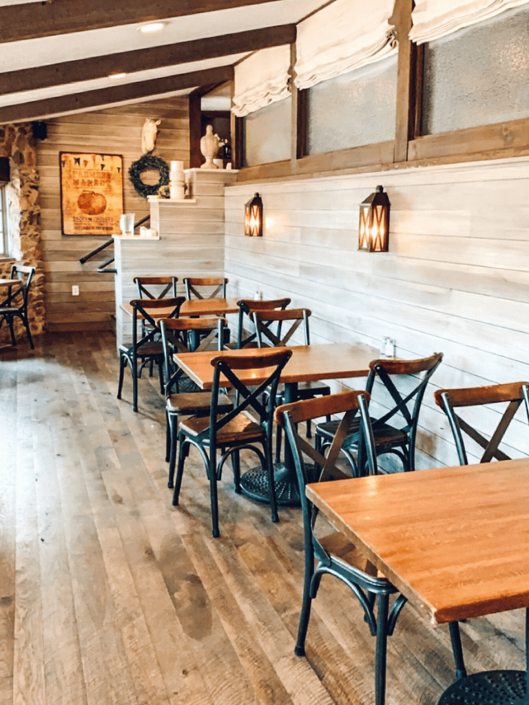 Cozy rustic restaurant interior with wooden dining tables and black cross-back chairs.