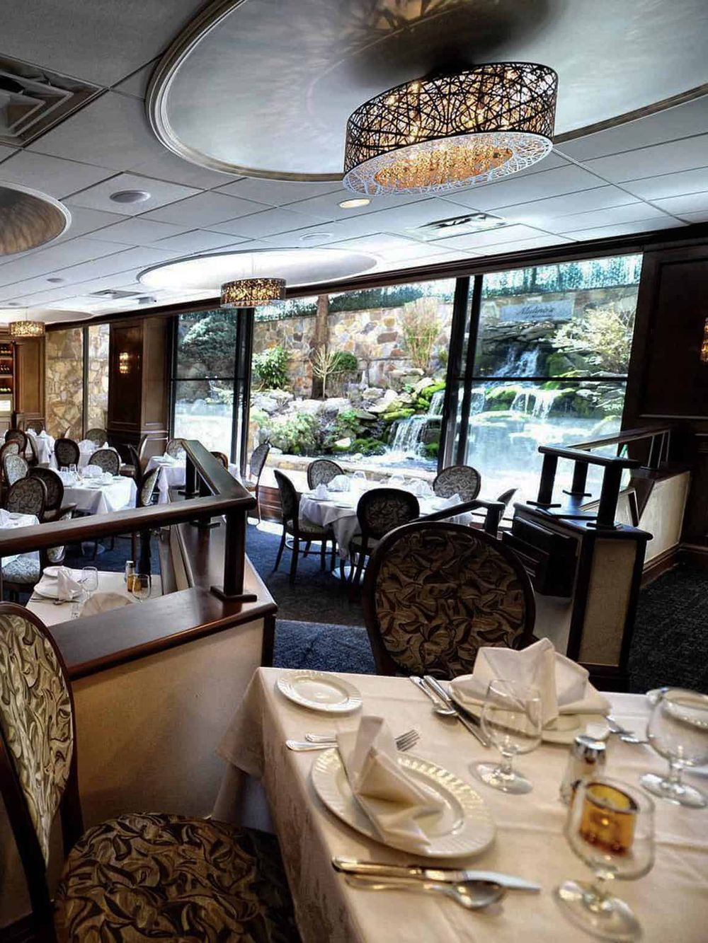 Elegant restaurant interior with large window view of waterfall and landscaped garden, ideal for fine dining and special occasions.