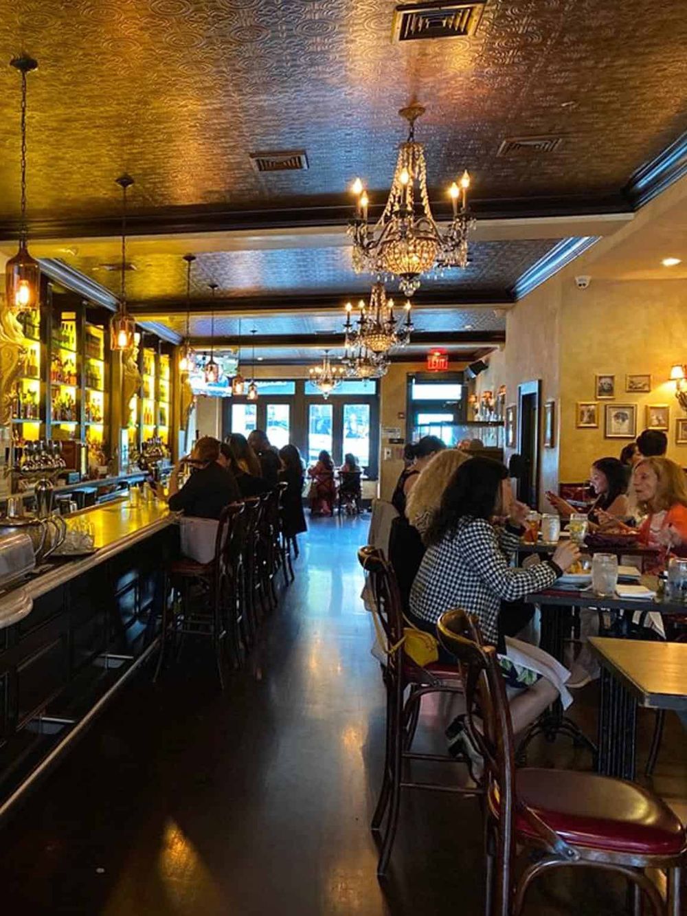 Elegant restaurant interior with chandeliers, bar seating, and customers dining; cozy ambiance and stylish decor.