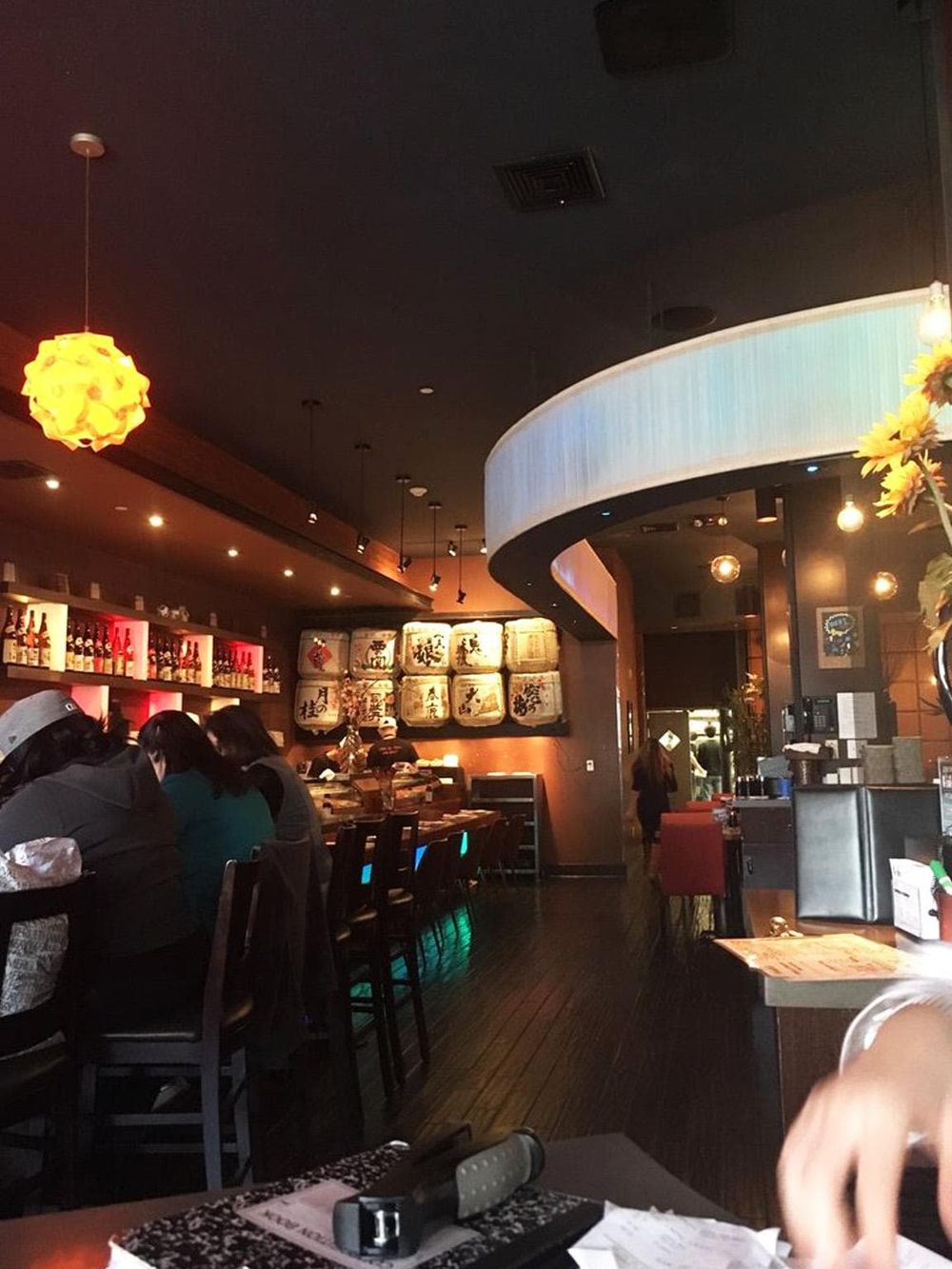 A cozy Japanese restaurant interior with bar seating, warm lighting, and traditional decorations with sake barrels.