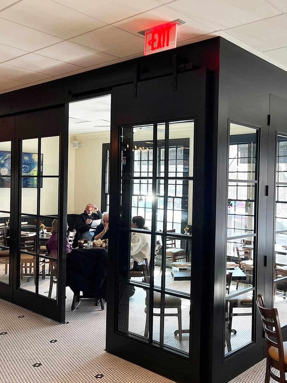 Modern restaurant interior with glass partition walls and diners enjoying their meals.