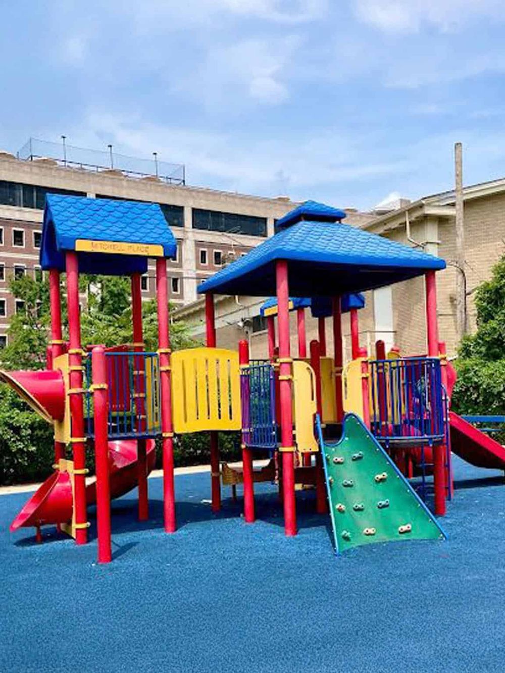 Bright colorful kids playground with slides, climbing wall, and roofs on a soft blue surface in an urban setting.