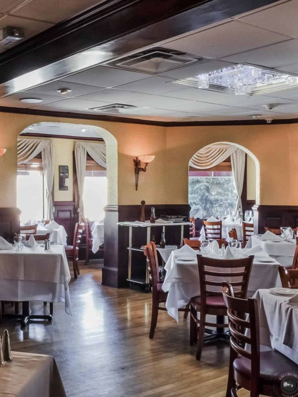 Bright, elegant restaurant interior with white tablecloths, wooden chairs, and classic decor.