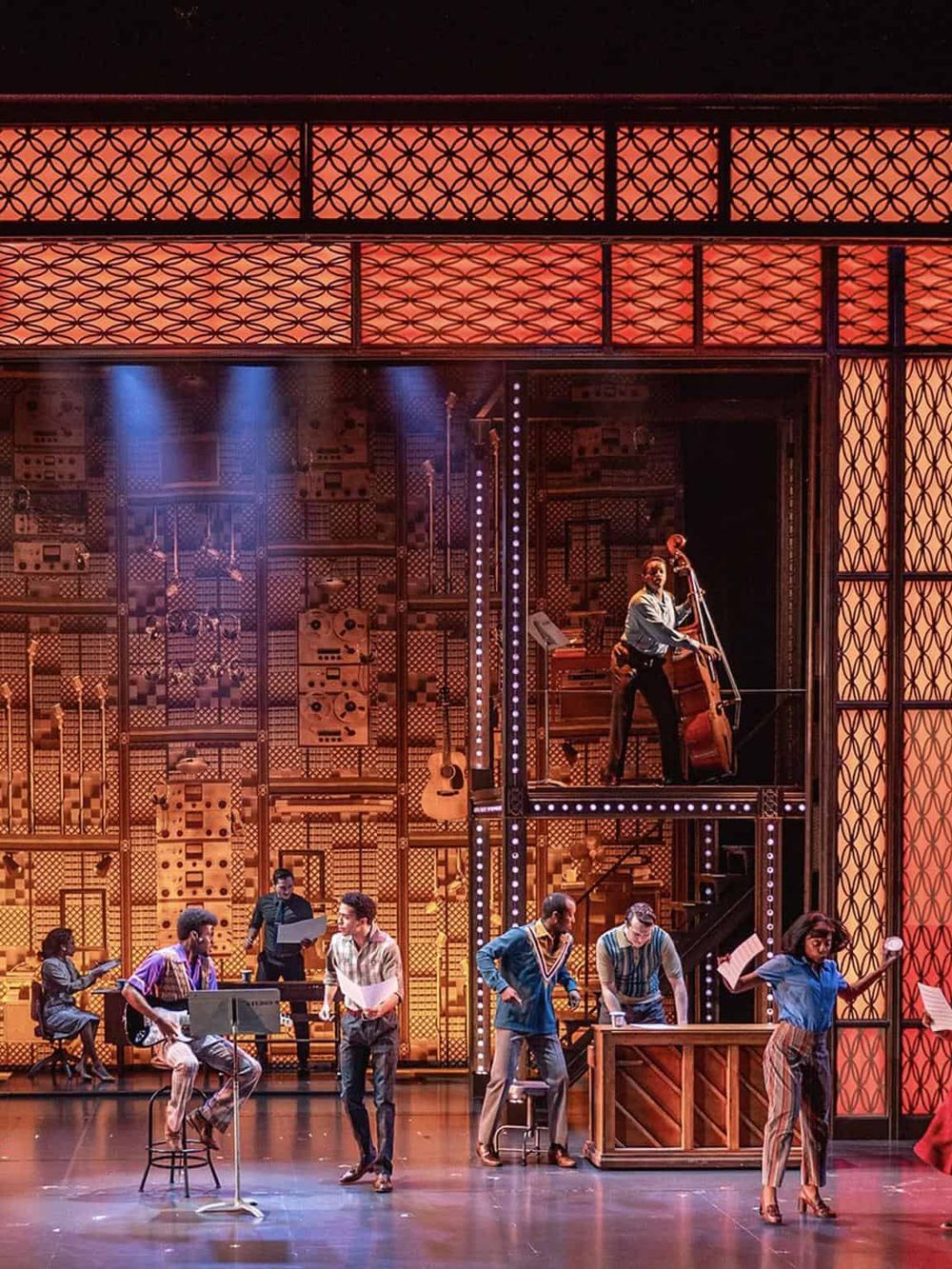Vibrant theater stage with musicians and actors performing in a colorful, dynamic set design.