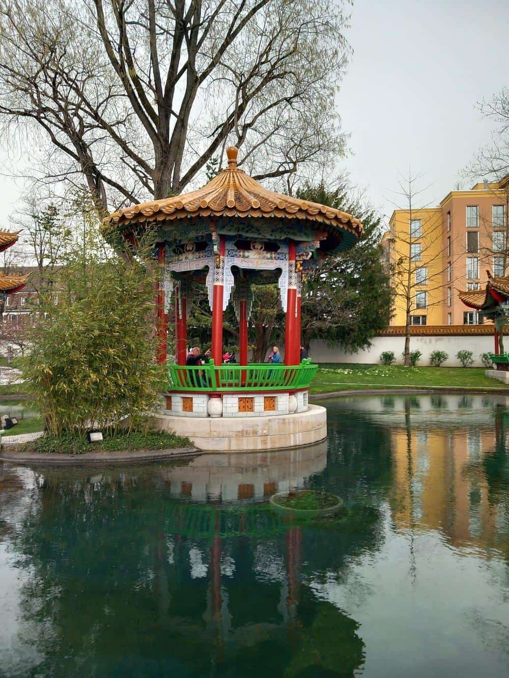 Colorful Asian-style pavilion in a scenic park with water reflection, perfect for tranquility and relaxation.